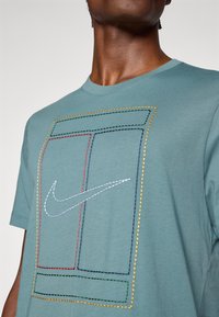 Τιρκουάζ βαμβακερό T-shirt με ραμμένο σχέδιο που περιλαμβάνει ορθογώνια σε κόκκινο, κίτρινο, πράσινο και μπλε χρώμα, καθώς και το λευκό λογότυπο της Nike στο κέντρο.