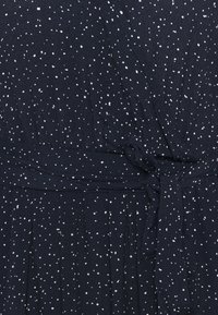 Tissu bleu foncé avec de petits pois blancs éparpillés et un détail de ceinture nouée à la taille.