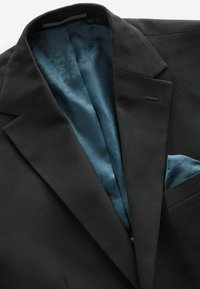 Blazer negro con un exterior texturizado, con un forro de patrón azul y un pañuelo en el mismo tono azul.