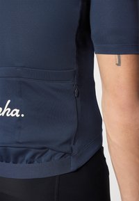 Camiseta deportiva azul marino de manga corta, con una textura sutil, bolsillo con cremallera y detalle en script blanco en la parte inferior delantera.