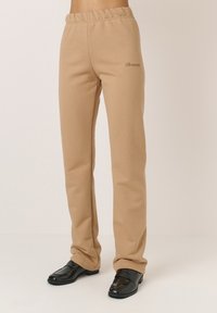 Beige szabadidőnadrág rugalmas derékrésszel, keskenyebb lábszárral és hímzett logóval. Sima anyag, puha tapintással.