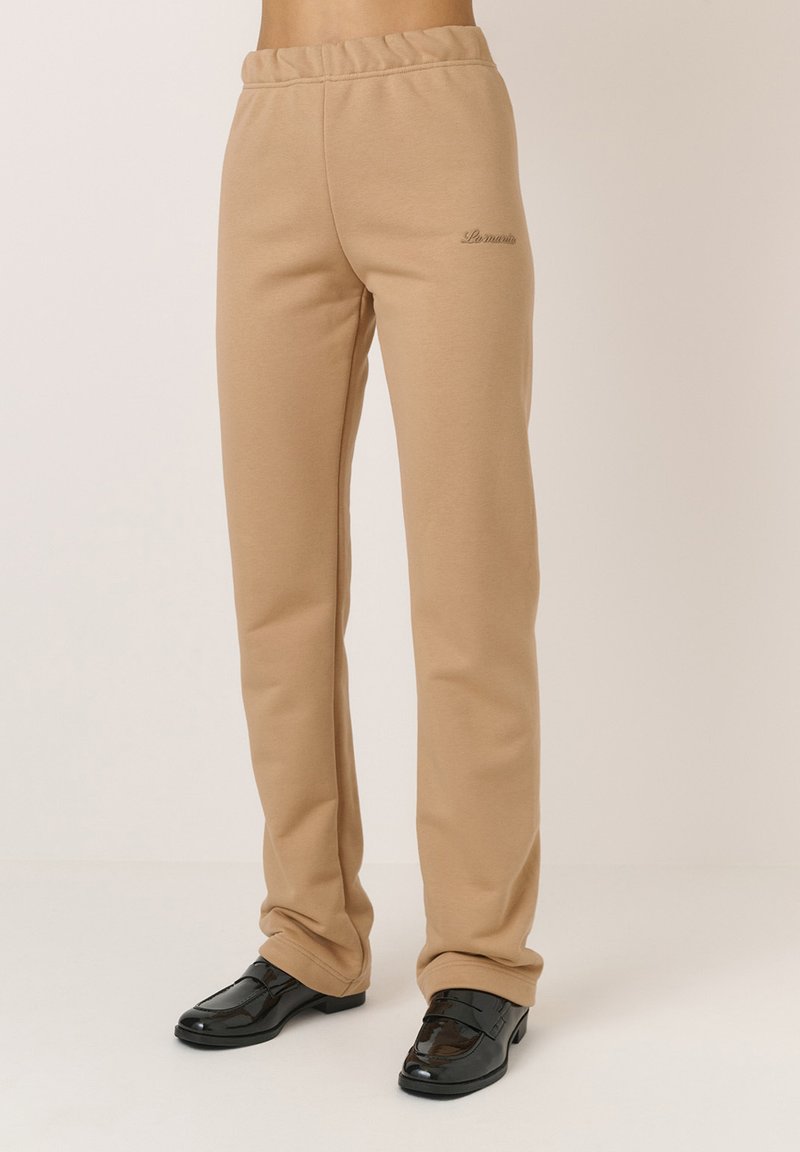 Beige szabadidőnadrág rugalmas derékrésszel, keskenyebb lábszárral és hímzett logóval. Sima anyag, puha tapintással.