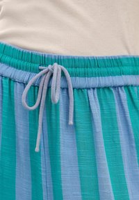 Ceinture d'un pantalon rayé bleu et vert avec un cordon de serrage bleu clair noué en un nœud sur un haut côtelé beige.