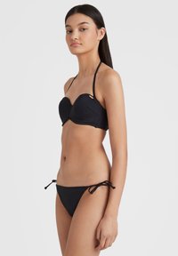 Melna bikini komplekts ar strukturētu, ieklātu augšu ar kakla saitēm un regulējamiem sāninekiem. Gluda tekstūra, minimālists dizains.