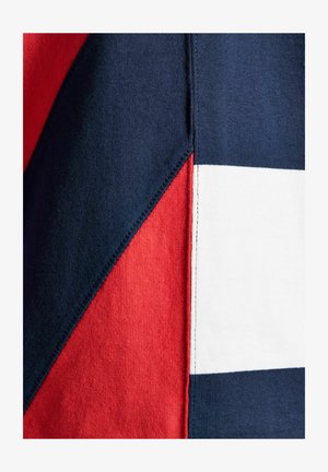 Nahaufnahme von Stoffpaneelen, die in Marineblau, Rot und Weiß zusammengenäht sind und geometrische Formen bilden.