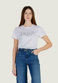 White cotton T-shirt featuring a rhinestone-embellished logo "LIU J" on the front, paired with high-waisted blue denim jeans.