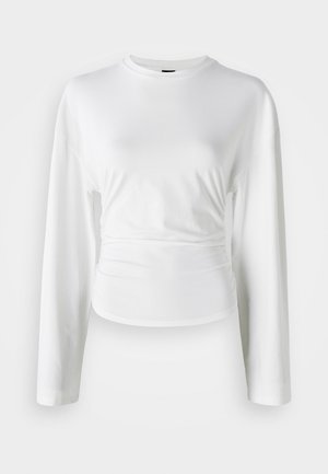 Camicia bianca a maniche lunghe realizzata in tessuto morbido. Presenta un design aderente con dettagli arricciati in vita e un collo rotondo.