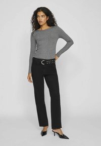 Camiseta gris de manga larga combinada con jeans negros de pierna recta. Acabado con un cinturón negro con tachuelas y tacones negros de punta. Textura simple.