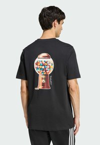 Černé tričko s barevnou grafikou automatu na žvýkačky na zádech, s ilustrací žvýkaček a lesklým kovovým víkem.