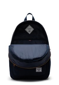 Zaino navy con parte superiore curva, tasca frontale con pattina e zip dorata. Presenta una fodera a righe e un'etichetta con logo all'interno.