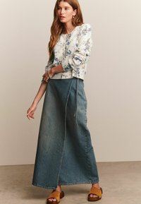 Pull léger à motifs floraux avec un col rond, associé à une longue jupe en denim bleu dotée d'un cordon de serrage et d'une silhouette décontractée. Sandales brunes.