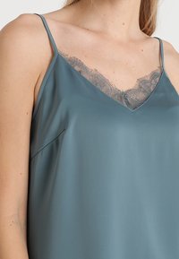 Camisole en satin bleu sarcelle à fines bretelles et encolure en V, ornée d'une délicate bordure de dentelle le long de l'encolure pour plus de texture et de détails.