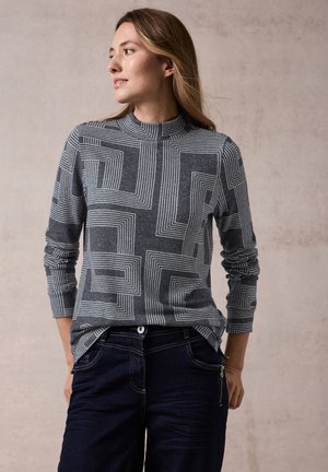 Haut gris à manches longues avec un motif géométrique à lignes blanches, col roulé côtelé et coupe décontractée, assorti à un pantalon en denim foncé.