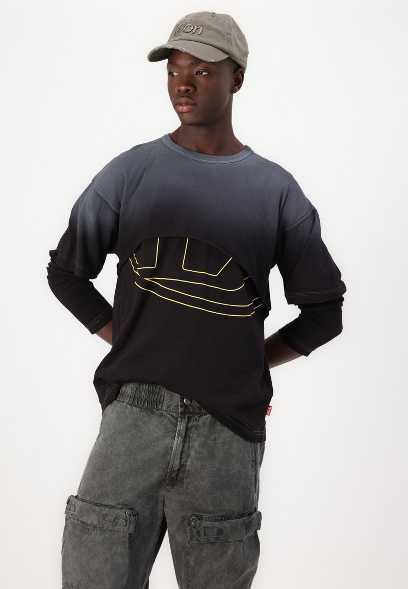 Czarna i szara koszula z długim rękawem o unikalnym kroju, zdobiona żółtą grafiką, połączona z szarymi spodniami cargo z kieszeniami i luźnym krojem.