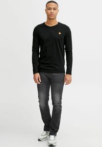 Black long-sleeve shirt with a rounded neckline, paired with dark gray jeans. Notable logo on the shirt and white sneakers with gray accents.