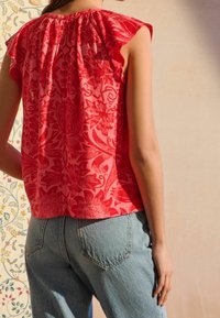 Haut sans manches à motif floral rouge avec encolure froncée, associé à un jean en denim bleu clair. Tissu doux avec une coupe décontractée.