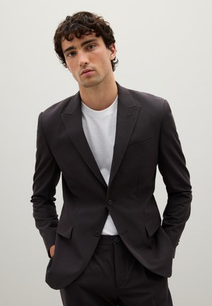 Traje entallado gris oscuro con blazer de un solo botón, solapas en pico y dos botones, combinado con una camiseta blanca de cuello redondo debajo.