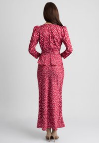 Długa różowa sukienka w białe kropki, z bufiastymi rękawami, peplum w talii i dopasowaną sylwetką, w zestawieniu z cielistymi szpilkami.