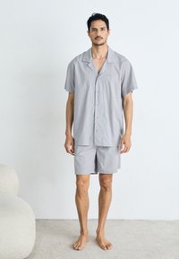 Svetlošedý pyžamový set s krátkym rukávom vyrobený z mäkkej látky, obsahujúci košieľku na gombíky a zodpovedajúce šortky. Minimalistický dizajn bez vzorov.