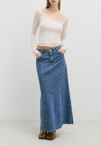 Licht beige langarm top met een een-schouder ontwerp, gecombineerd met een blauwe denim maxi rok met een rechte snit en een rafelige zoom.