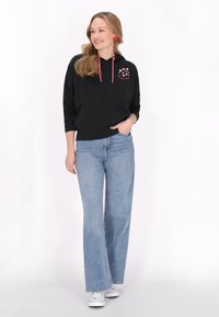 Sudadera negra con cordones rosa, bordado floral en el pecho, combinada con jeans de pierna ancha de color azul claro y zapatillas blancas.