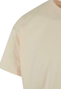 Bež pamučna majica s kratkim rukavima, okruglim izrezom i glatkom teksturom. Minimalistički dizajn, bez vidljivih uzoraka ili akcenata.