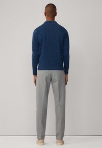 Blauwe gebreide trui met geribde zoom en mouwen, gecombineerd met lichtgrijze pantalon en beige schoenen, gezien vanaf de achterkant.