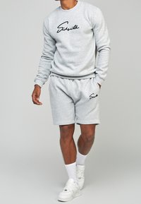 Felpa grigia con logo a script nero sul davanti, abbinata a pantaloncini grigi coordinati e sneakers bianche. Tessuto liscio, vestibilità comoda.