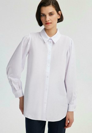 White long-sleeve shirt made of smooth fabric, featuring a button-down front, classic collar, and gathered detailing at the shoulders.