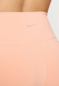 High-waisted pink leggings with a smooth texture, featuring a small, light gray Nike logo on the waistband and flatlock stitching.