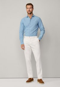 Chemise boutonnée bleu clair en coton, associée à un pantalon blanc et des mocassins bruns ; design simple, silhouette ajustée, sans motifs.