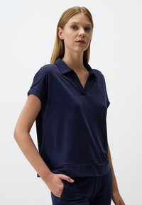 Marineblauwe polo met korte mouwen, in een ontspannen pasvorm, met een v-hals en zachte, gestructureerde stof. Minimalistisch ontwerp zonder patronen.