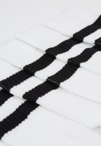 Weiße Socken mit drei auffälligen horizontalen schwarzen Streifen, geripptem Ausdruck und einem gefalteten Design für eine einfache Aufbewahrung.