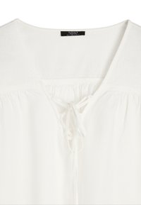 Biała bluzka uszyta z lekkiego materiału, charakteryzująca się głębokim dekoltem w serek, marszczeniem poniżej dekoltu oraz sznurowanym zapięciem z przodu.