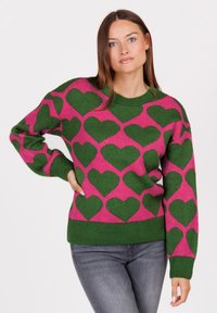 Maglione lavorato a maglia con una base rosa e modelli a cuore verdi, scollo a girocollo a coste e polsini. Il tessuto sembra morbido e strutturato.
