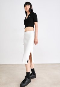Čierny rebrovaný top s krátkym rukávom v kombinácii s bielou rebrovanou midi sukňou so bočným rozparkom. Model má na sebe čierne tenisky a ponožky.