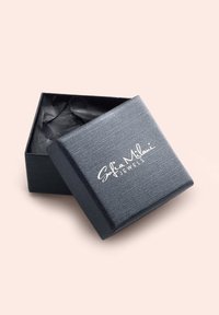 Svart smyckeskrin med en strukturerad yta och silverlogotyp. Ligger något öppet och avslöjar veckat svart silkepapper inuti.