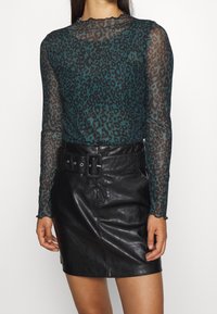 Genomskinlig teal långärmad topp med svart leopardmönster, tillsammans med en höga midjan svart läder mini kjol och ett brett bälte som accent.