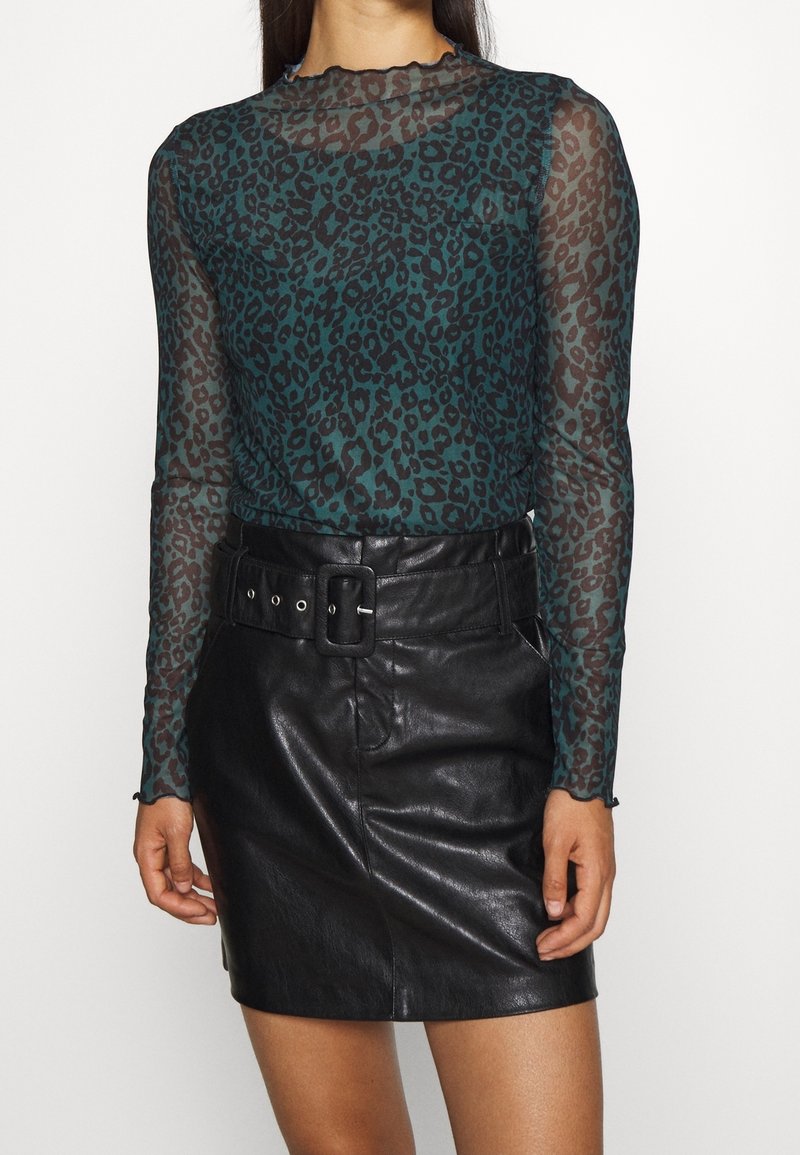 Genomskinlig teal långärmad topp med svart leopardmönster, tillsammans med en höga midjan svart läder mini kjol och ett brett bälte som accent.