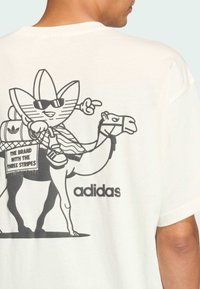 Witte katoenen t-shirt met een zwart grafisch ontwerp van een personage met grote zonnebril op een kameel. "adidas" logo onderaan.