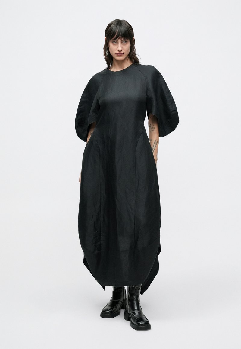 Vestito nero dalla vestibilità ampia, maniche larghe e scollatura rotonda, realizzato in tessuto strutturato. Abbinato a stivali platform neri.