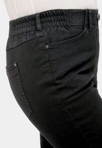 Schwarze Denim-Hosen mit elastischem Bund, die eine glatte Textur und Seitentaschen aufweisen. Schlanker Schnitt mit subtilen Nähdetails.