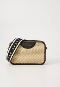 Beige värjätty käsilaukku mustilla nahkakiinnikkeillä, päällä vetoketjulla ja mustavalkoisella merkkipainatuksella varustetulla hihnalla. Kompakti ja suorakaiteen muotoinen.