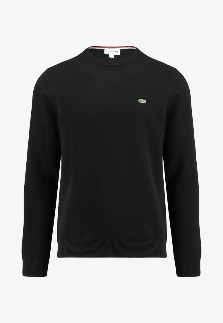 Svart stickad tröja med rund hals, prydd med en liten grön krokodil-logga på bröstet samt ribbade ärmslut och nederkant. Mjuk textur.