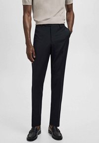 Pantalones negros de corte ajustado, diseño de frente plano, tejido ligero, ajuste entallado, combinados con una camisa beige y mocasines negros, textura suave.