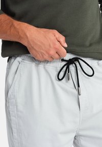 Shorts elásticos de cintura en gris claro con cordón negro y acentos metálicos, que presentan bolsillos laterales y una textura suave.