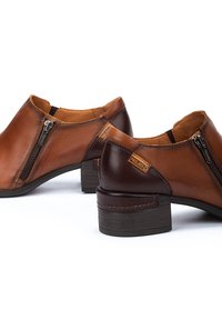 Bottines en cuir marron avec un petit talon en bois, dotées de fermetures éclair latérales et de patchs marron contrastants sur le dessus. Fini texturé et lisse.