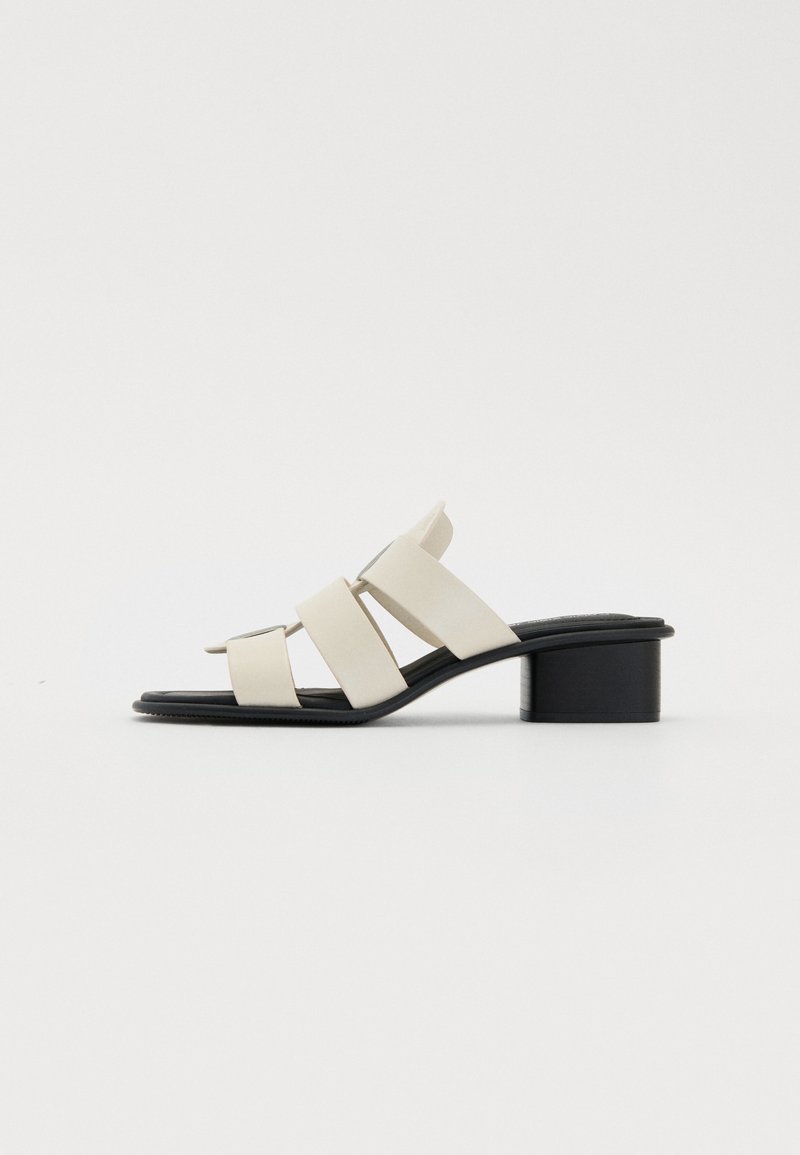 Sandales pour femmes avec une tige synthétique beige clair et trois larges brides. Talon bloc noir, dos ouvert et semelle intérieure lisse.