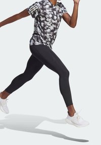 Leggings deportivas negras combinadas con una camiseta de tie-dye en blanco y negro que presenta tres rayas blancas en la manga izquierda, llevadas con zapatillas blancas.