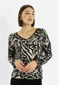 Haut à manches longues avec col en V présentant un imprimé animalier noir et crème. Tissu doux avec des embellissements dorés subtils et des poignets côtelés.